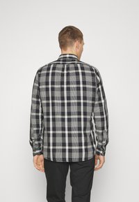 Czarna i biała koszula w kratę, wykonana z bawełny, z długimi rękawami, tradycyjnym kołnierzem i mankietami na guziki, z kontrastującym wzorem kratki na plecach.