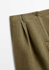 Olive green linen trousers featuring front pleats, a button closure, and a side pocket. Smooth texture with a relaxed fit.