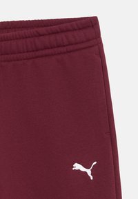 Bordowe dresy z elastycznym pasem, z białym haftowanym logo po lewej dolnej stronie. Miękka tekstura i minimalistyczny design.