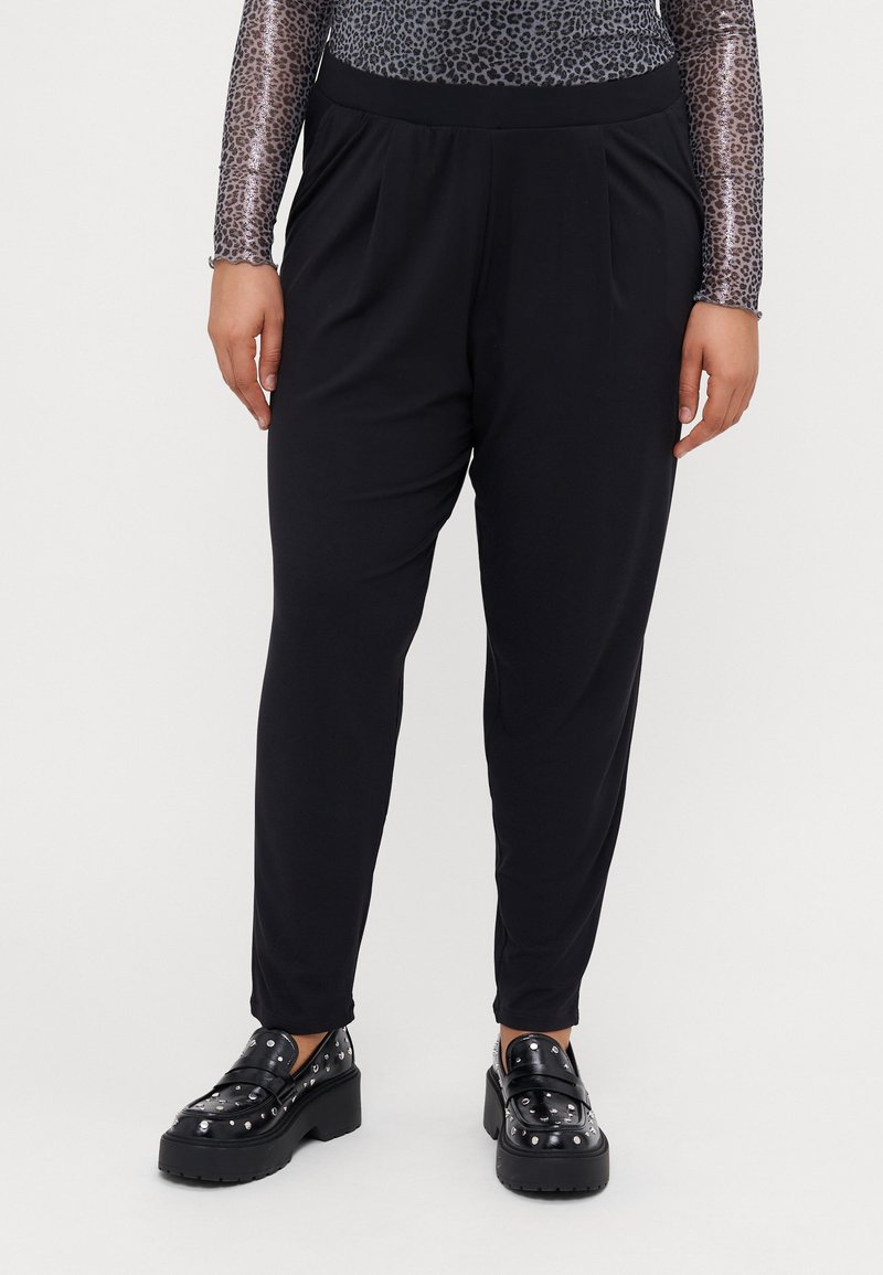 Personne portant un pantalon noir fuselé, un haut à manches longues à imprimé animal et des mocassins à plateforme noirs avec des clous argentés.