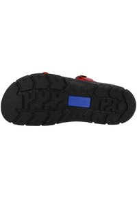 Black rubber sole with deep treads for traction, featuring a blue label. Shows a rounded heel and a wider front for stability.