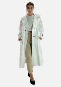 Biała trench coat z dużymi klapami, podwójnym zapięciem na guziki i czarnymi akcentami guzikowymi. Noszona na krótką białą bluzkę i beżowe spodnie.