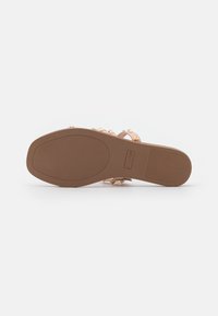 Semelle en caoutchouc marron avec des rainures, ornée d'accents de clous en ton doré. Les brides transparentes présentent une texture lisse, offrant stabilité et soutien.