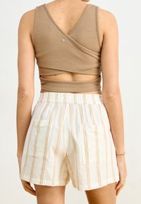 Débardeur en tan avec un tissu texturé et un dos en V ; associé à un short blanc à rayures beige verticales et à poches avant.