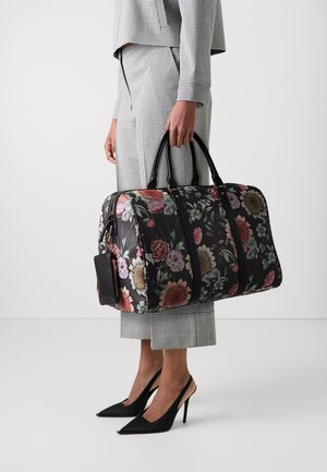 Black floral duffel bag with multicolored flowers, zipper top closure, dual handles, and a detachable small pouch. Textured fabric finish.