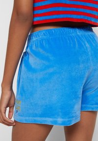 Světle modré sametové šortky s elastickým pasem a bočními kapsami, s vyšitým nápisem "Tommy Jeans" ve žluté barvě. Hladký povrch.