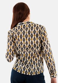 Camisa de manga larga con un diseño estampado en negro, amarillo y blanco. Confeccionada en una tela suave, con cuello y puños abotonados.