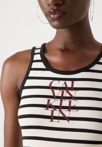 Black and white striped tank top with a black trim and multicolored "CALVIN KLEIN" logo in a bold font at the center. Smooth texture.