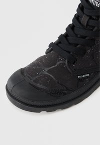 Černé plátěné boty s šedým skvrnitým vzorem, gumovou špičkou a černými tkaničkami. Mají texturovanou podrážku a značkování po straně.