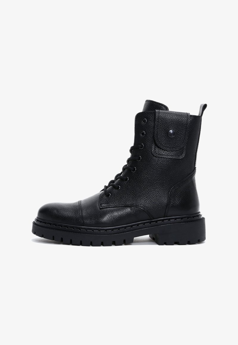 Bota de combate de cuero negro con cordones, suela gruesa con tacos y un pequeño bolsillo con botón a presión en el eje, vista lateral sobre fondo blanco.