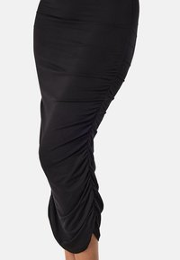 Jupe noire en tissu extensible, dotée de fronces sur le côté pour ajouter de la forme et de la texture. Fini lisse et silhouette ajustée.