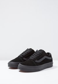 Sneakers in suede nera con accenti grigi, caratterizzati da un design a bassa altezza, punta rotonda e lacci texturizzati. La suola è in gomma nera solida.