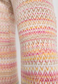 Knitted fabric featuring a repeating zigzag pattern in shades of pink, yellow, and beige on a light background; soft texture.