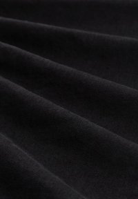Tela negra con una textura suave, que presenta múltiples pliegues que crean sombras y profundidad, resaltando su estructura ligera y flexible.