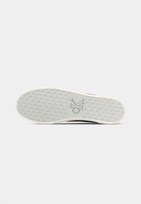 White rubber shoe sole featuring a textured grip pattern, with a logo "CK" embossed near the heel and a contrasting color trim.