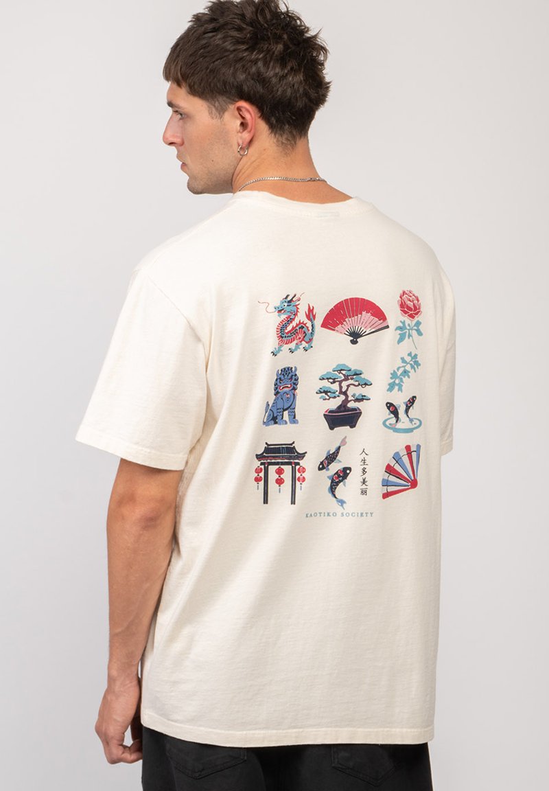 Mężczyzna noszący kremowy t-shirt z kolorowymi, inspirowanymi Azją wzorami, takimi jak smok, wachlarz, drzewko bonsai, ryba koi i brama latarniowa na plecach.