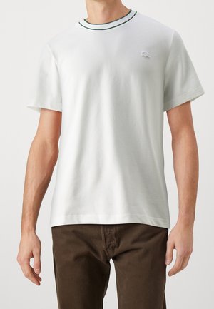T-shirt en coton blanc avec un col rond orné de finitions vertes, des manches courtes et un petit logo brodé sur la poitrine.