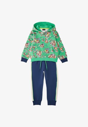 Chaqueta verde con capucha y cremallera con estampado de mono de tenis divertido combinada con pantalones jogger azul marino con rayas blancas en los laterales y cintura con cordón.