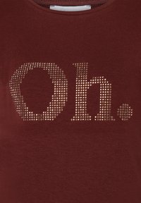 Burgunderrotes T-Shirt mit Rundhalsausschnitt, das ein aus Strasssteinen gestaltetes Design zeigt, das "Oh." in einer auffälligen, dekorativen Schriftart buchstabiert.