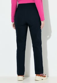 Granatowe spodnie o prostym kroju, z elastycznym pasem i gładką fakturą, zestawione z jasnymi sportowymi butami ozdobionymi kwiatowym wzorem.