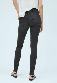 Jeans negros ajustados de cintura alta, con bolsillos en la parte trasera y una textura suave. Combinados con sandalias planas.