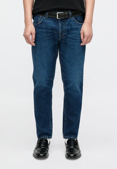 Τζιν με ίσια γραμμή σε μεσαίο μπλε denim, με πέντε τσέπες, φερμουάρ και διακριτική ξεθώριαση. Φοριέται με μαύρη ζώνη και παπούτσια.