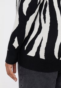 Μαύρο και άσπρο πουλόβερ με μοτίβο ζέβρας, φτιαγμένο από πλεκτό ύφασμα, με ριγέ τελείωμα και μανσέτες που έχουν μαλακή υφή.