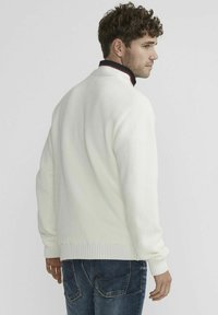 Witte gebreide trui met een gestructureerd patroon, geribbelde boorden en zoom, met een contrasterende zwarte en rode kraag. Draag over blauwdenim jeans.