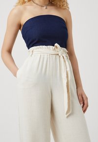 Haut bustier bleu marine associé à un pantalon large en lin crème, doté d'une taille ceinturée et d'une texture douce.