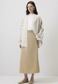 Cardigan bej din in, stil kimono, cu broderie intricate, asortat cu o fustă solidă bej cu talie elastică și încălțăminte plată simplă.