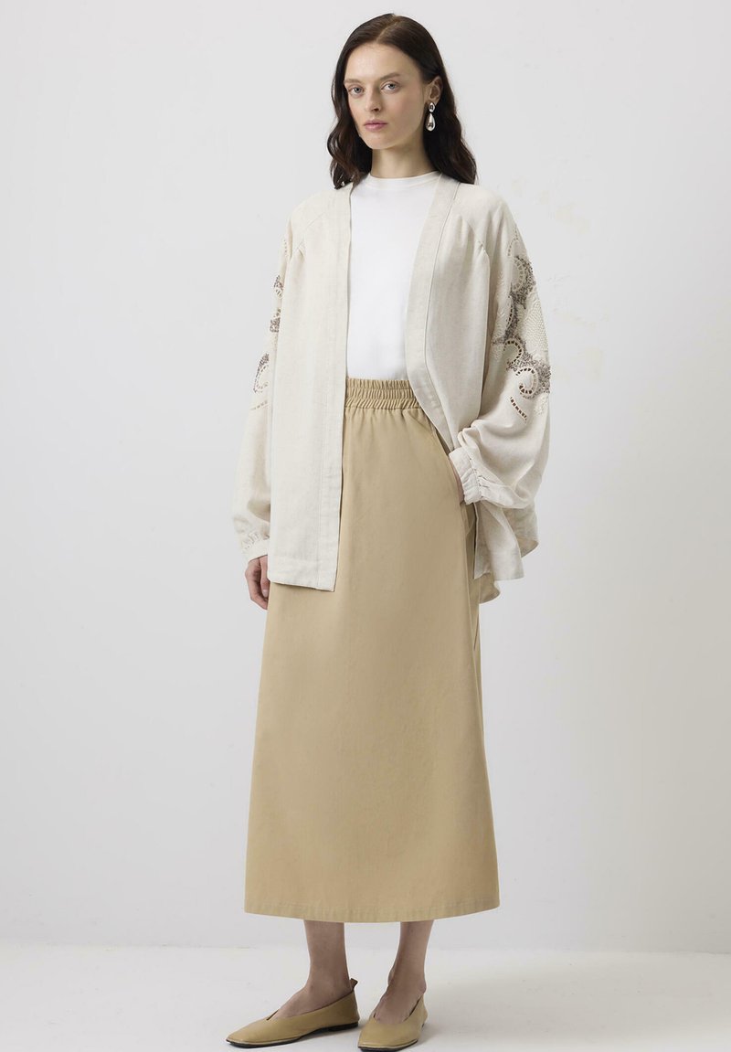Cardigan bej din in, stil kimono, cu broderie intricate, asortat cu o fustă solidă bej cu talie elastică și încălțăminte plată simplă.