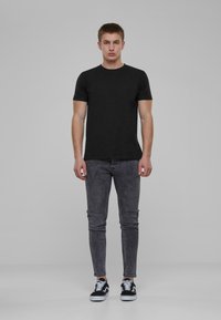 Fekete, rövid ujjú póló, karcsú szabású sötétszürke farmernadrág és fekete, fehér részletekkel ellátott sportcipő; minimalista design és sima textúra.