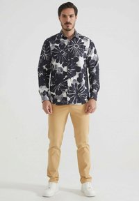 Chemise à manches longues à motifs floraux navy et blancs avec fermeture à boutons, associée à un pantalon slim beige clair et des baskets blanches.