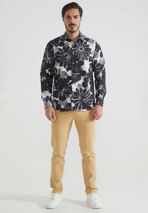 Chemise à manches longues à motifs floraux navy et blancs avec fermeture à boutons, associée à un pantalon slim beige clair et des baskets blanches.