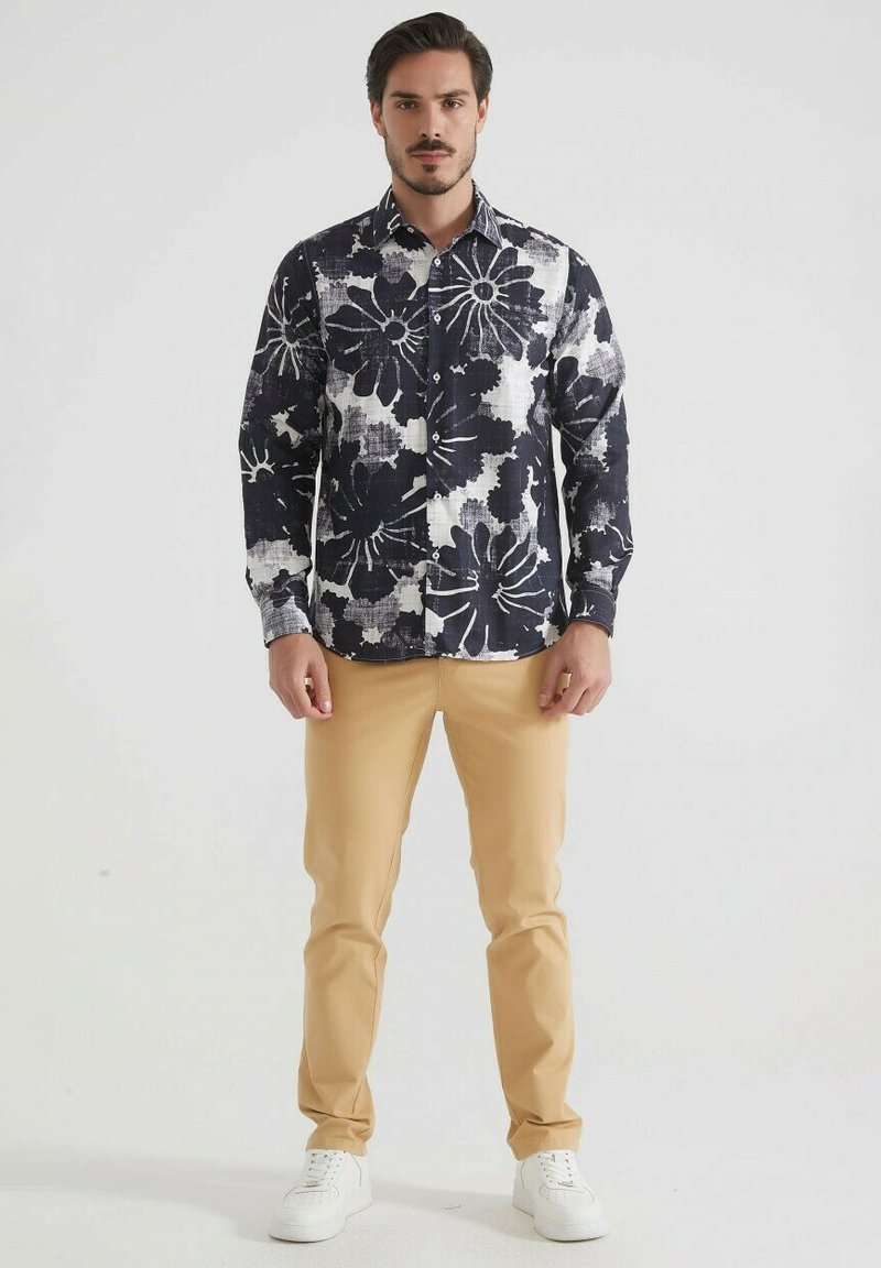 Chemise à manches longues à motifs floraux navy et blancs avec fermeture à boutons, associée à un pantalon slim beige clair et des baskets blanches.