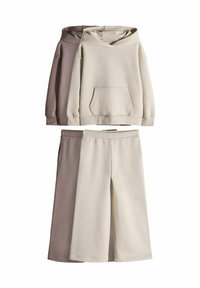 Dos sudaderas en beige claro y topo, con un bolsillo frontal y un corte relajado, combinadas con pantalones cortos beige claros con una cintura elástica.