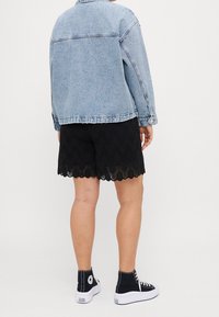 Lichtblauwe spijkerjas, gecombineerd met zwarte kanten shorts met gegolfde randen, en zwarte hoge sneakers met witte zolen.