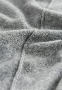 Grau stoff mit einer weichen, strukturierten Oberfläche. Sichtbare Nähte und Falten erzeugen ein sanft drapiertes Aussehen, das an ein gemütliches, komfortables Kleidungsstück erinnert.