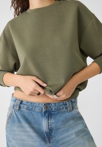 Olijfgroene sweatshirt met een relaxte pasvorm en driekwart mouwen, gecombineerd met lichtblauwe denim shorts. Soepele structuur, eenvoudig ontwerp.