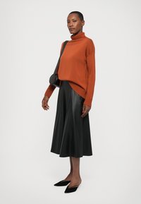 Rustfarget strikkegenser med høy krage, kombinert med et svart midi-skjørt i imitert skinn. Sorte spisse leiligheter og en liten svart crossover-veske.