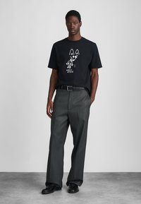 Fekete pamut póló fehér grafikával és rövid ujjal, szürke pliszált nadrággal és fekete cipővel párosítva. Egyszerű, modern dizájn.