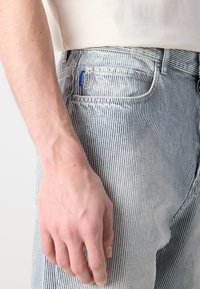 Világoskék csíkos farmernadrág finom textúrával. Hátul zseben kék márkajelzés található, klasszikus öt zsebes kialakítással.