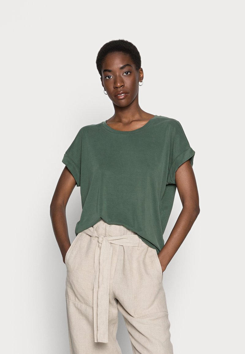 Green short-sleeve t-shirt in a soft material with a relaxed fit, round neckline, and rolled sleeves, paired with light beige trousers.