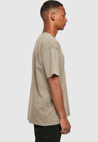 Kaki medvilnės marškinėliai trumpomis rankovėmis, su apvalia iškirpte ir laisvu siluetu. Su matomais siūlais ir šiek tiek nudėvėta tekstūra.