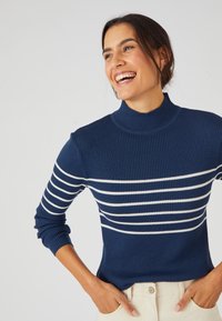 Maglione a costine blu navy con righe orizzontali bianche, collo alto e maniche lunghe. Texture liscia, design aderente, arricchito da uno stile minimalista.
