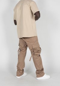 Camiseta de algodón beige combinada con pantalones cargo marrón claro que presentan múltiples bolsillos, lazos y piernas rectas. Llevado con zapatillas blancas.