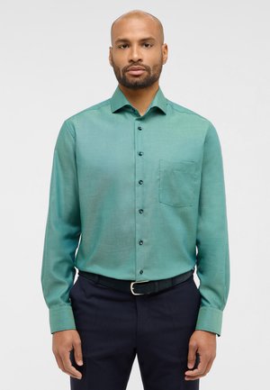 Green button-up shirt with a left chest pocket, long sleeves, and dark buttons, made of a smooth fabric, worn with dark pants.
