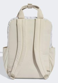 Mochila beige con tejido acolchado, correas anchas ajustables, asa superior para llevar y bolsillos laterales para almacenamiento adicional. Textura suave.