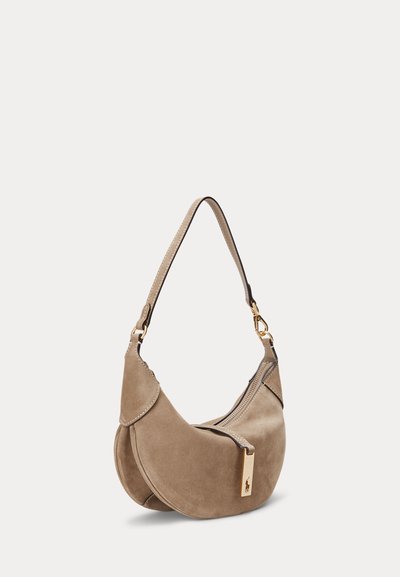 Kabelka z taupe semišu v tvare polmesiaca s jedným popruhom, horným zipsom a zlatým logom na ťaháčiku zipsu.