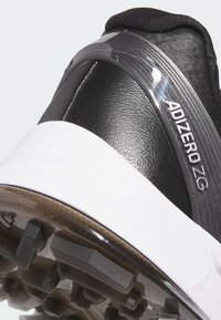 Close-up of a black and white sports shoe heel with textured sole and "ADIZERO ZG" branding on the side.